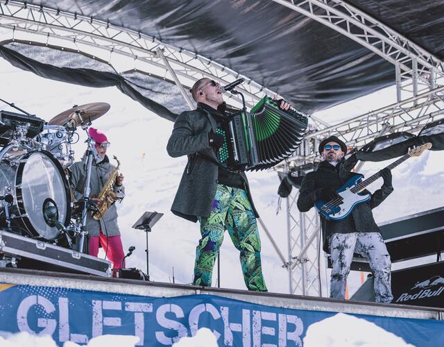 Band spielt auf Bühne im Schnee, Akkordeonspieler im Vordergrund