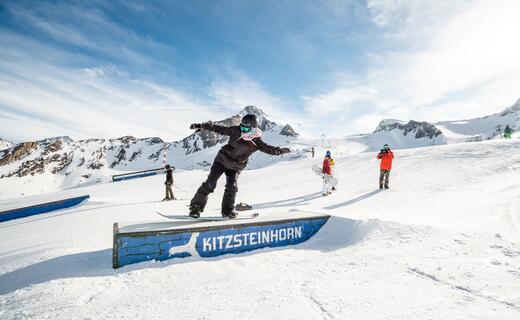 Snowboarder auf Rampe vor verschneiter Berglandschaft am Kitzsteinhorn